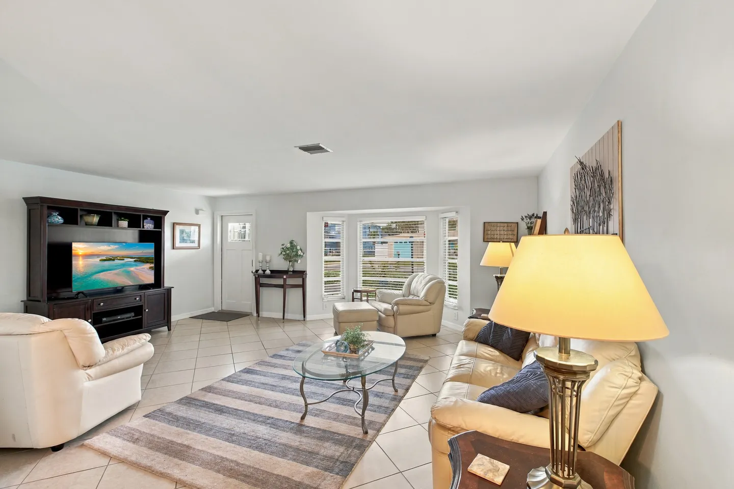 Spacious living room with light tile floors, leather seating, an entertainment center with a TV, and a bay window.