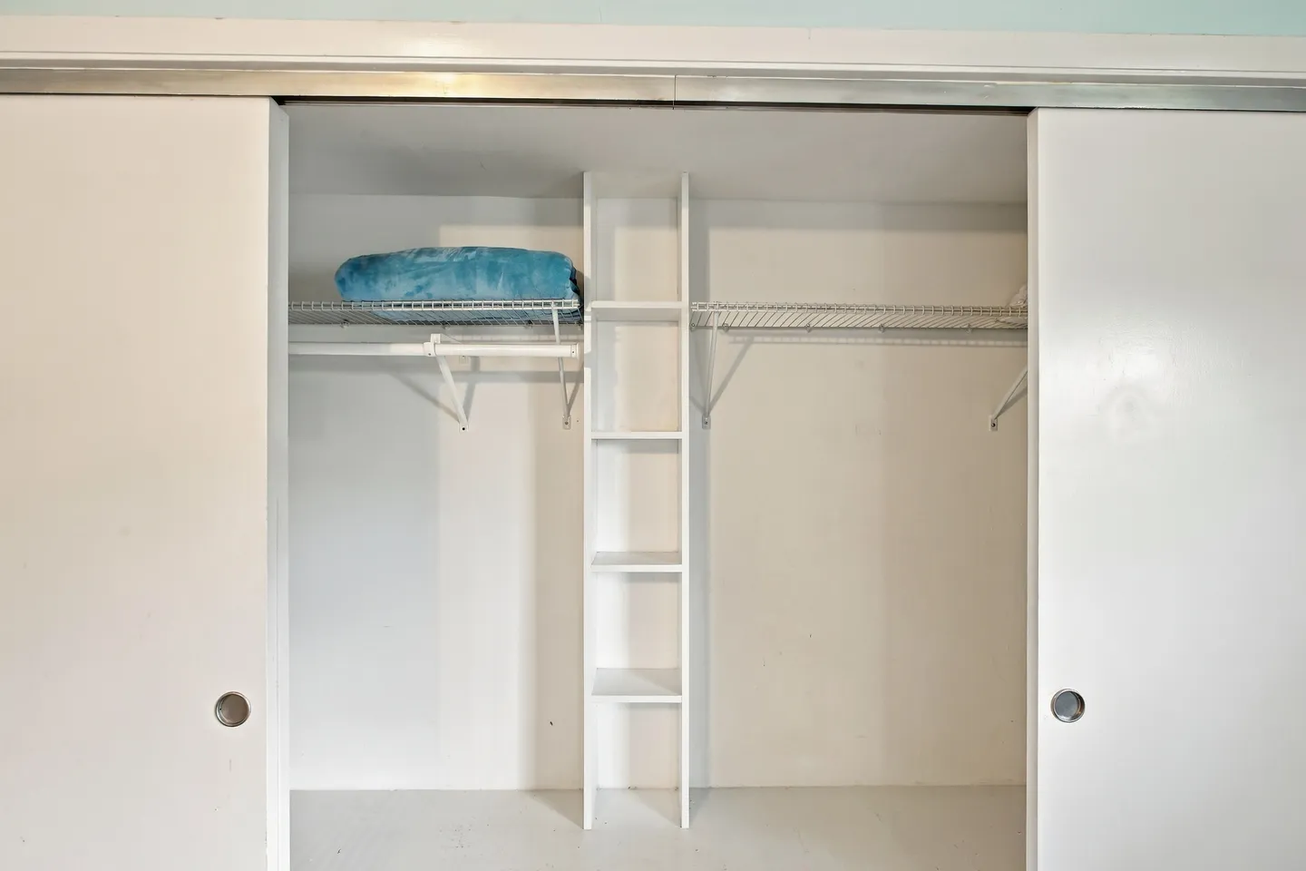 Open sliding closet doors revealing wire shelving, hanging rods, and a central vertical cubby organizer.