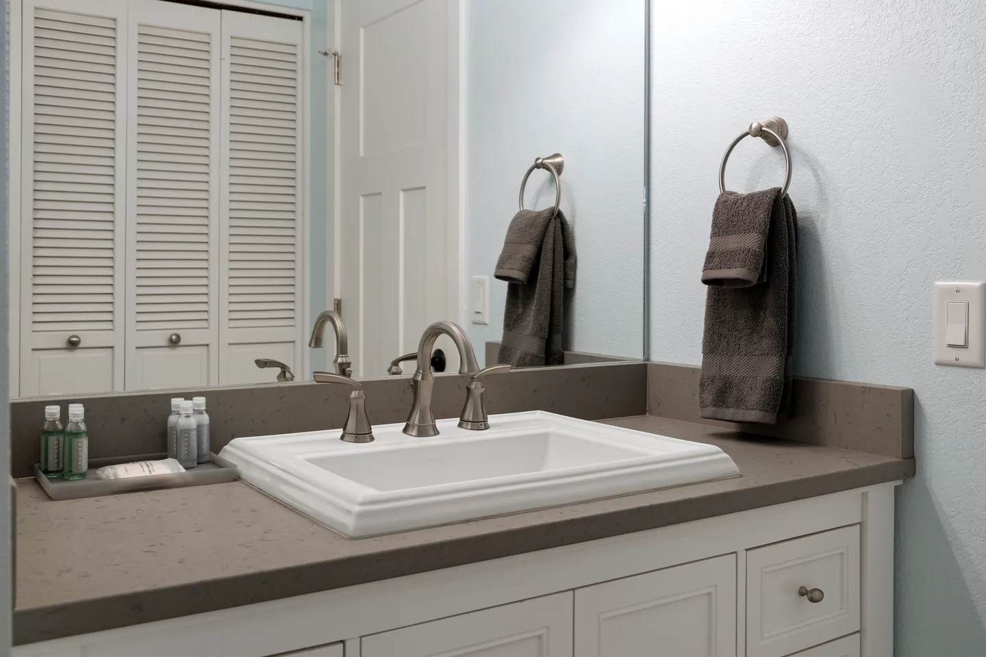 Bathroom vanity with a rectangular sink, brushed nickel faucet, large mirror, and hand towel ring.