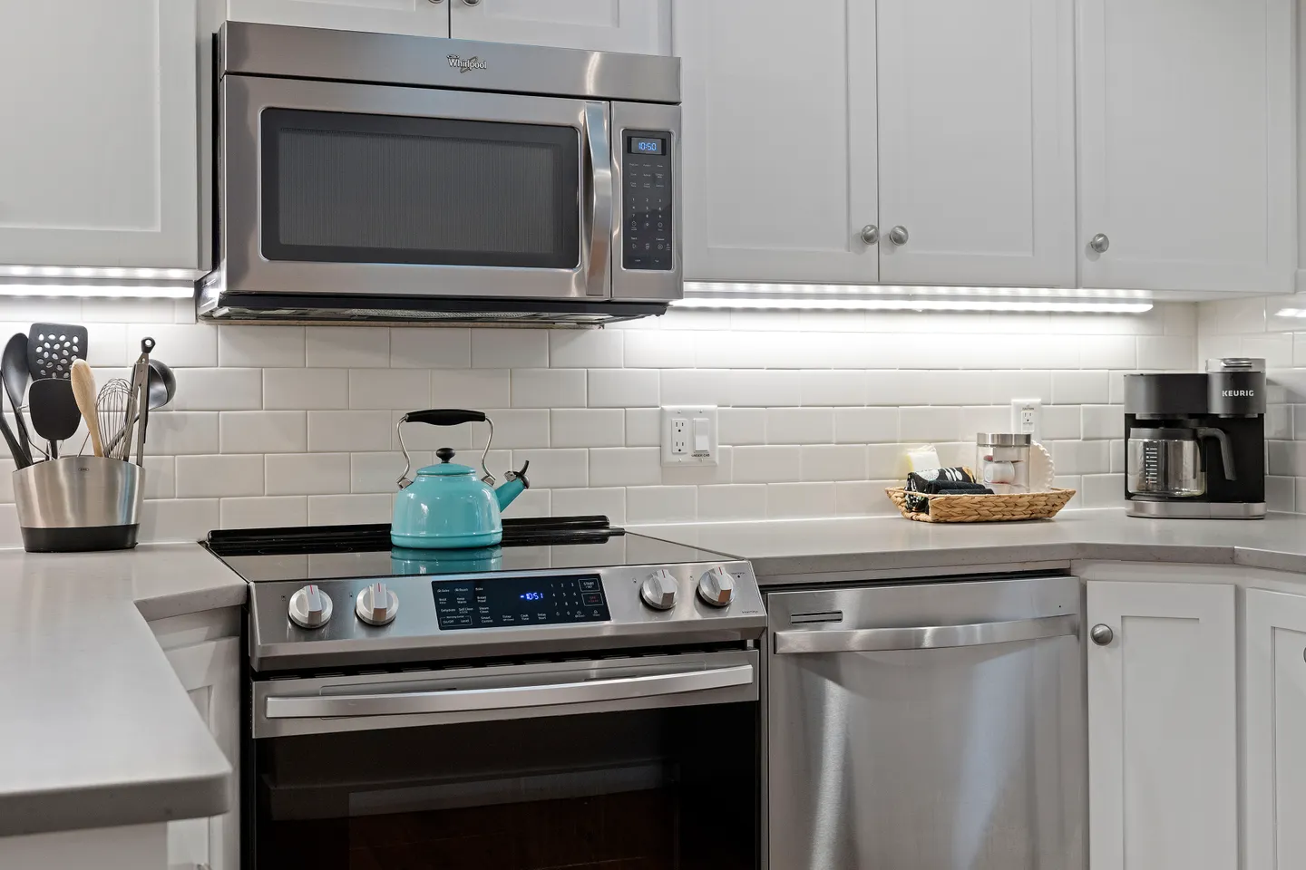 Kitchen counter featuring stainless steel appliances including an electric range, over-the-range microwave, and dishwasher with white cabinets.