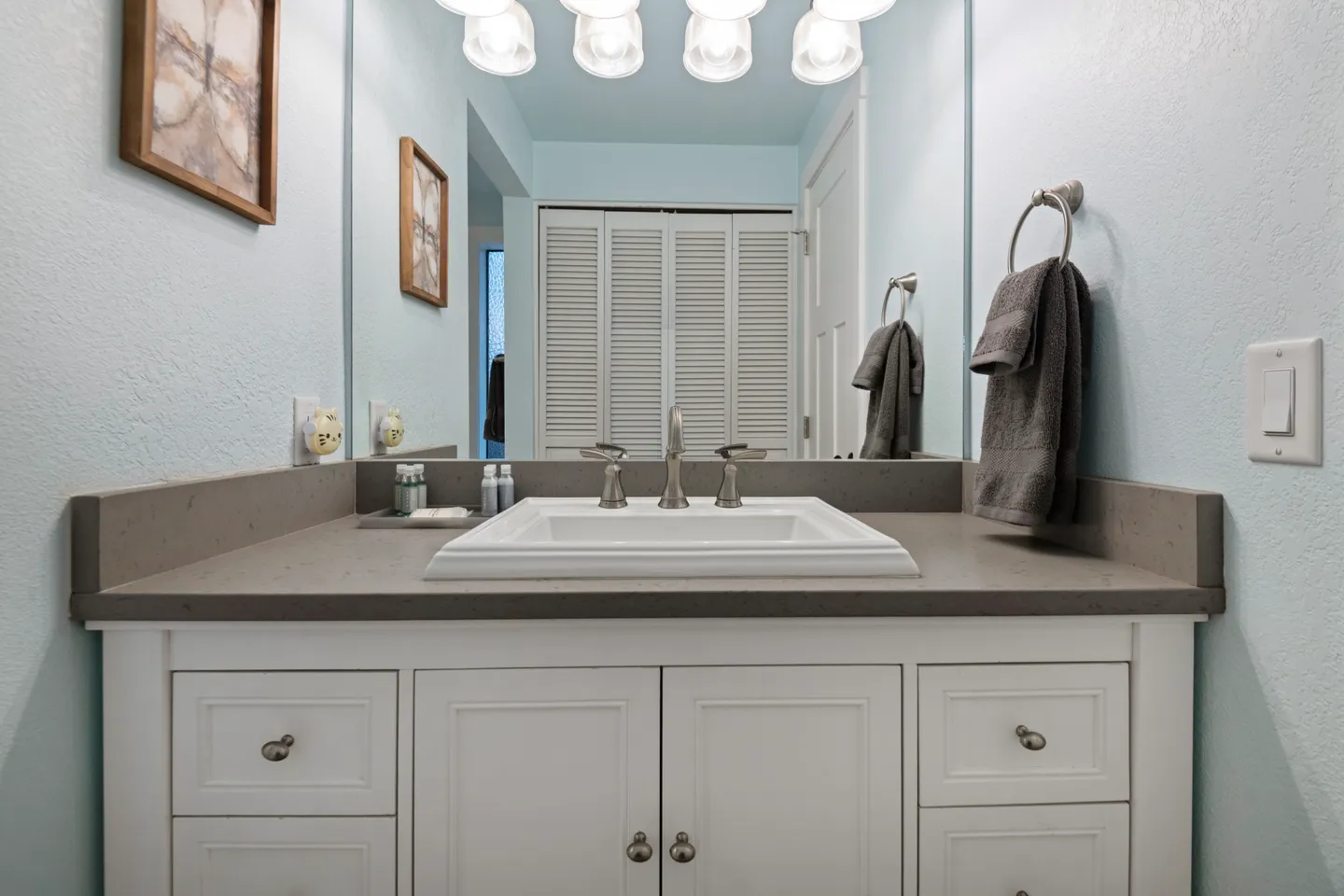 Bathroom vanity with a gray countertop, white rectangular sink, large mirror, and vanity lights.