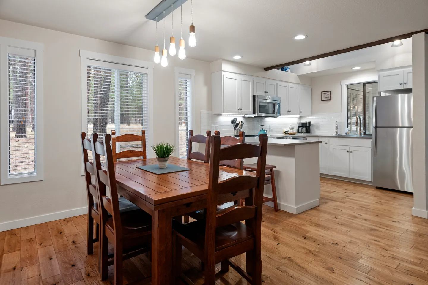 Dining area with a wooden table and chairs adjacent to an open-concept kitchen with white cabinets.
