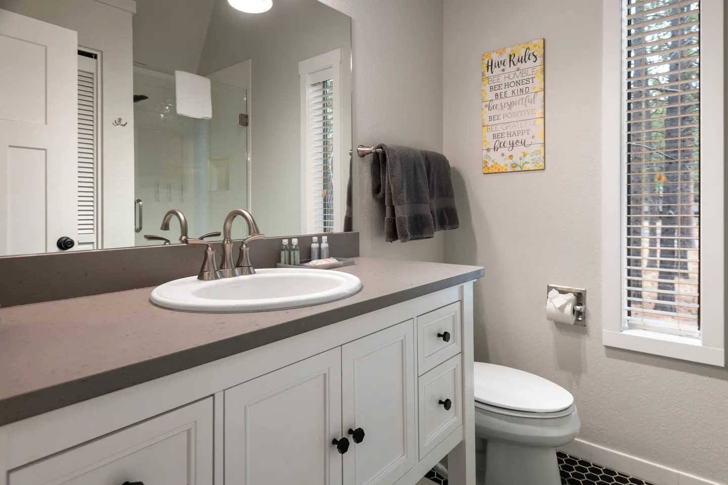 Bathroom vanity with an oval sink, dark countertop, white cabinets, and a mirror showing a glass shower.