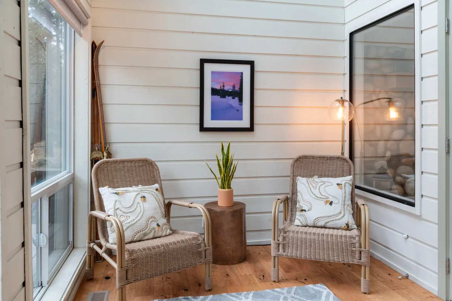 Sunroom corner with two woven armchairs, a small side table with a potted plant, and white horizontal paneled walls.