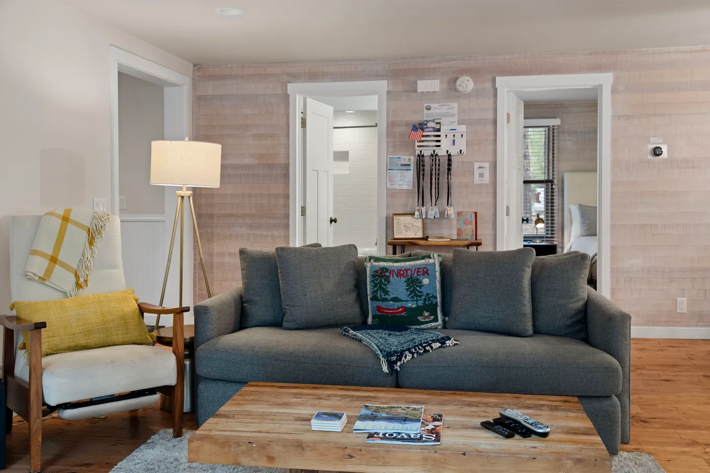 Living area featuring a gray sofa, wooden coffee table, armchair, tripod floor lamp, and doorways leading to other rooms.