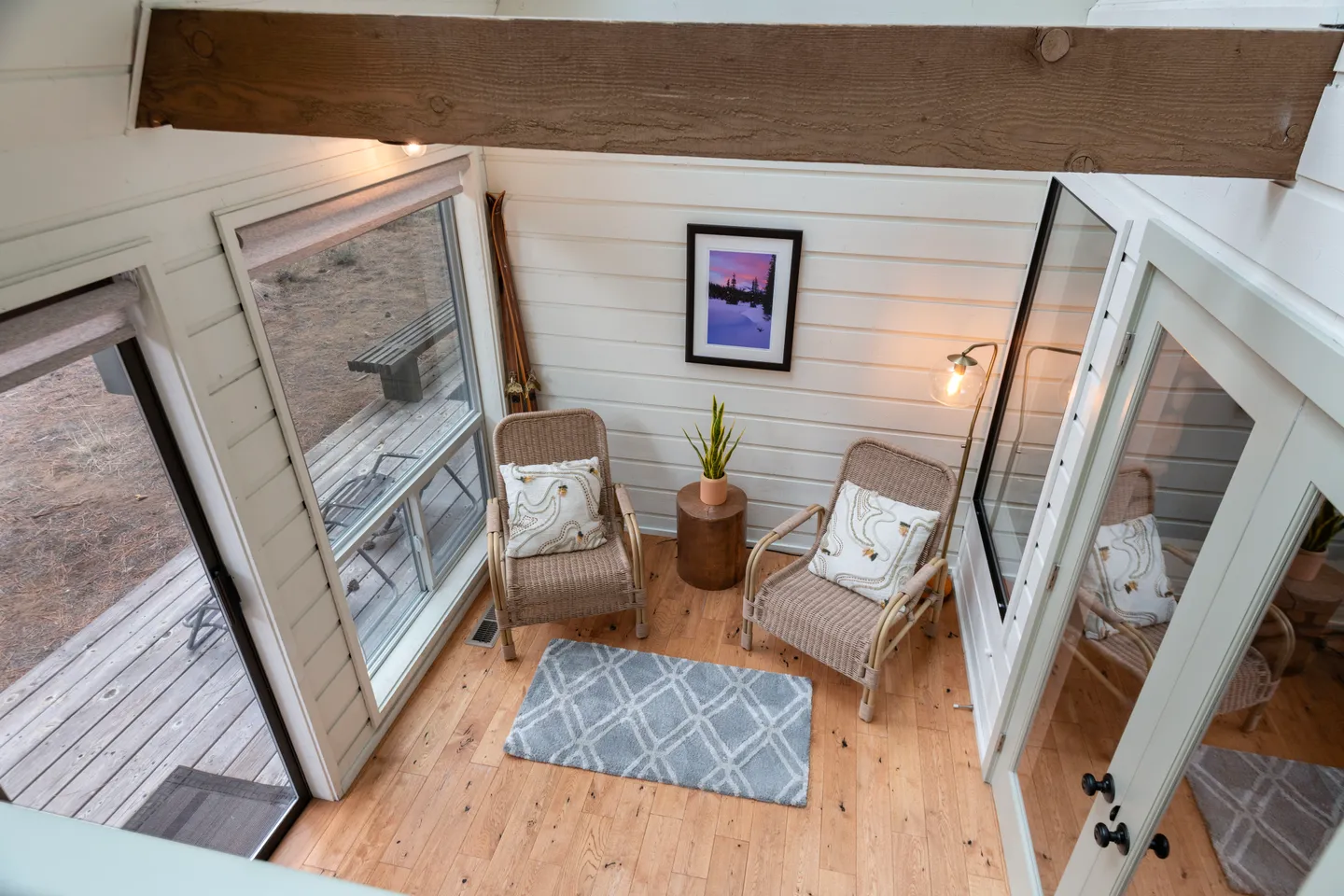 Sunroom seating area viewed from above with two wicker armchairs, wooden flooring, and large windows looking onto an outdoor deck.