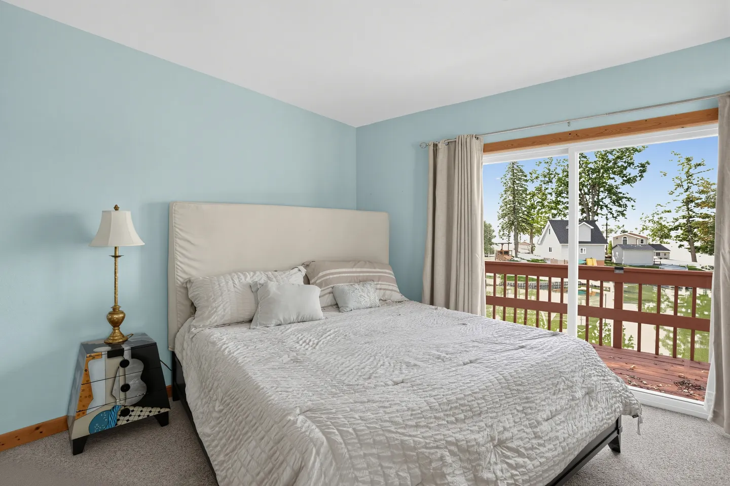 Bedroom with light blue walls, a bed with a light-colored upholstered headboard, and sliding glass doors leading to a balcony.