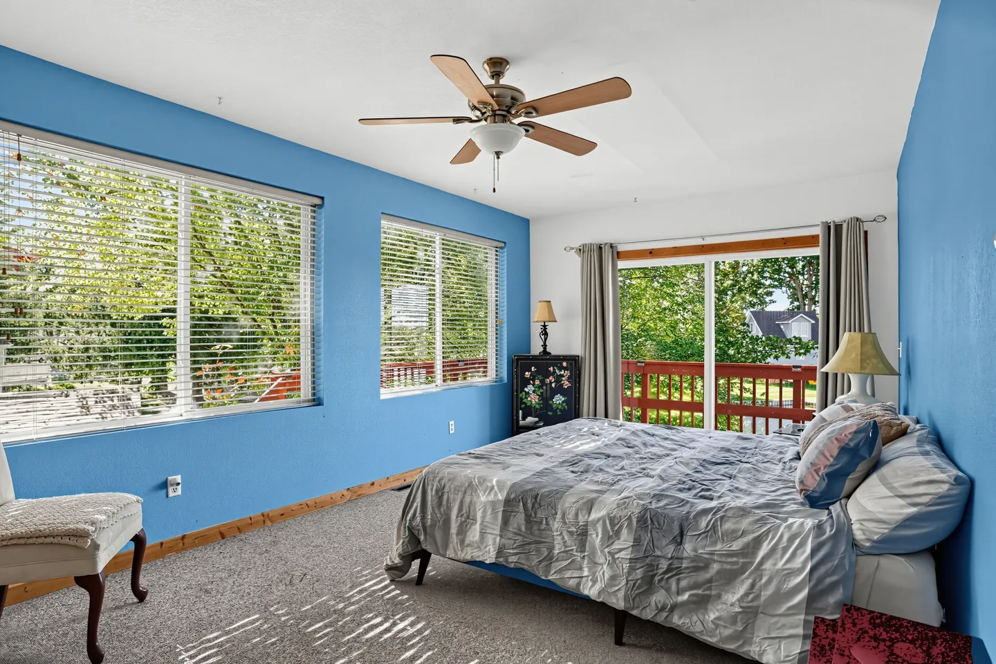 Bedroom with blue walls, carpeted floor, ceiling fan, bed, and sliding glass door leading to a balcony.