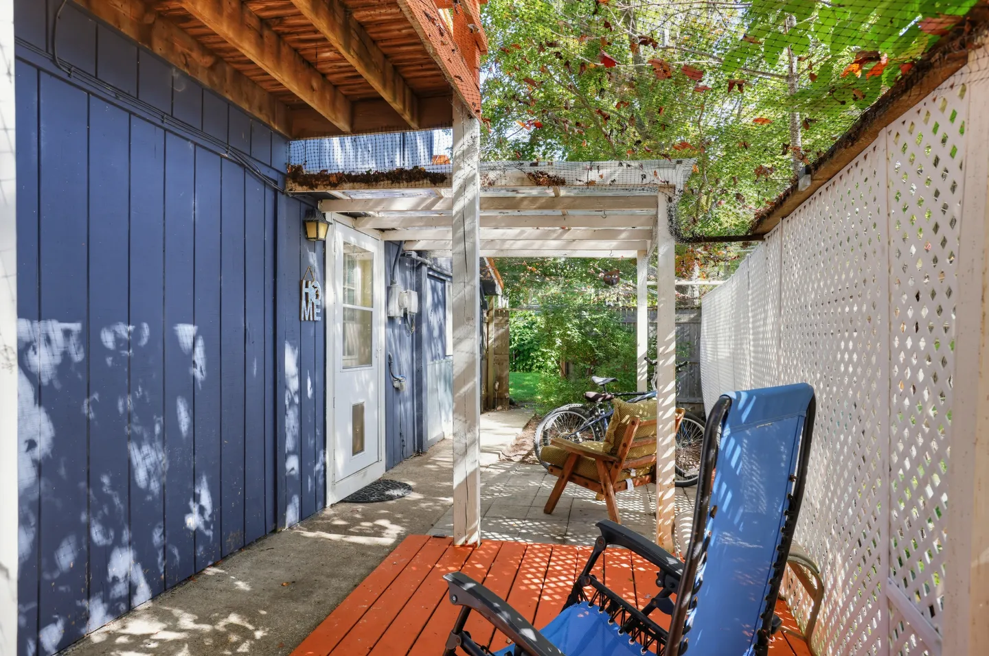 Outdoor side patio with blue recliner, wooden chair, pergola, lattice privacy fence, and bicycles.