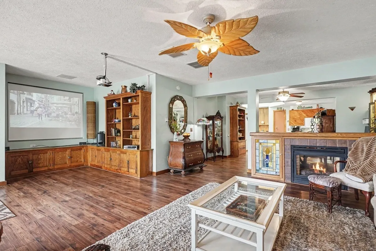 Living room with wood-style flooring, a projector and screen, built-in wooden cabinetry, and a fireplace.