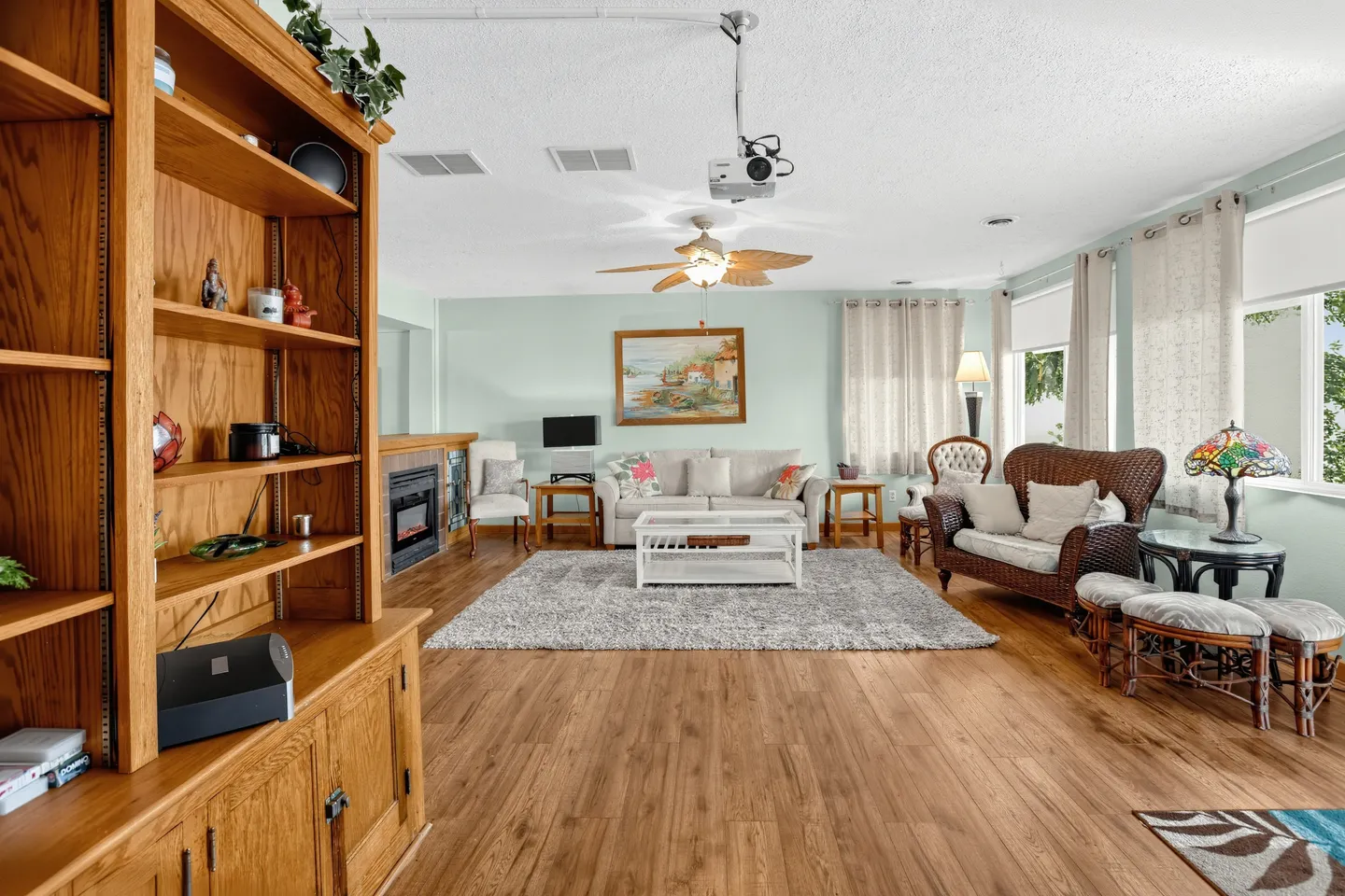 Living room with wood-look floors, a ceiling-mounted projector, a sofa, wicker seating, and a large wooden entertainment bookcase.