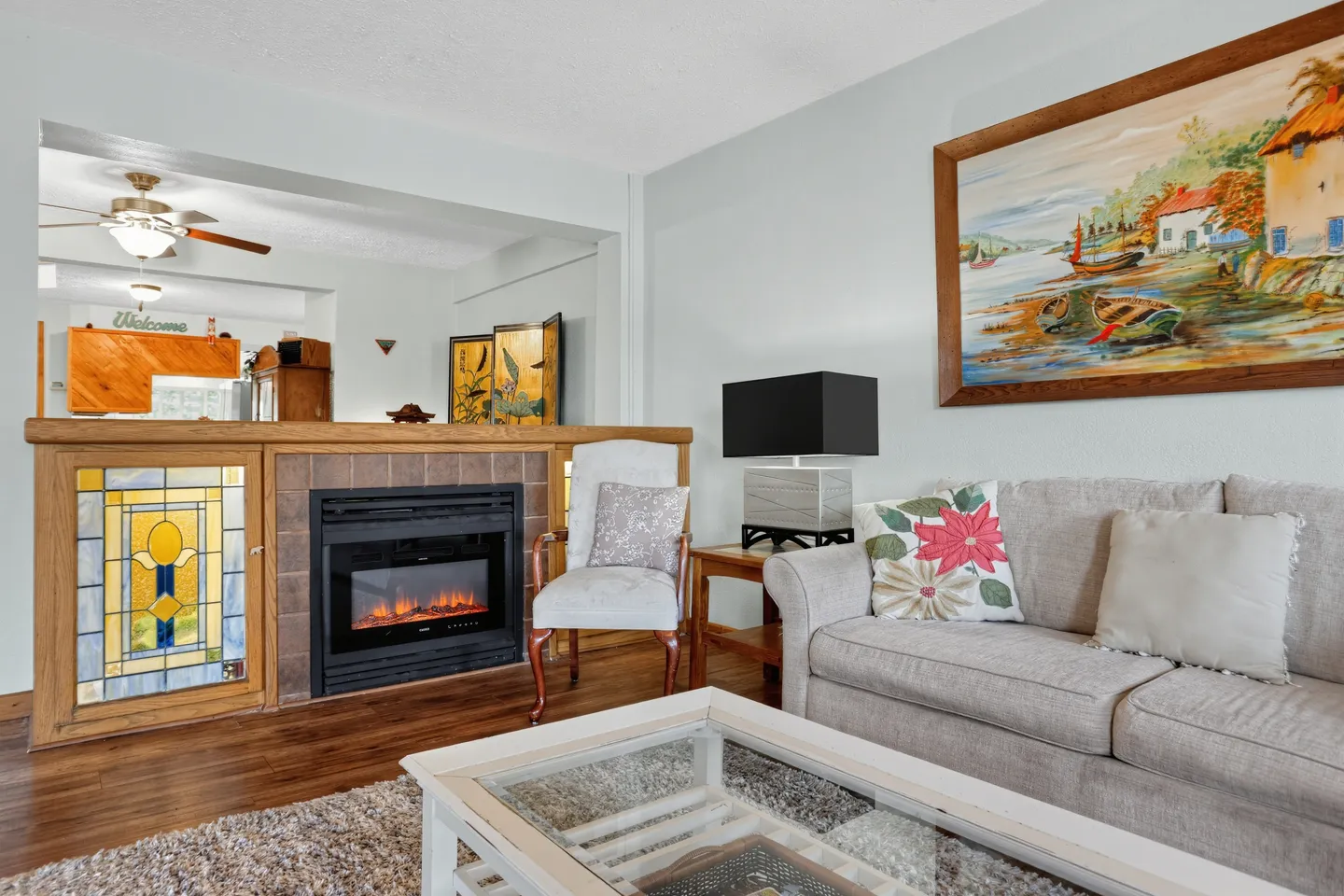 Living room with an electric fireplace, stained glass accent panel, sofa, armchair, and framed painting on the wall.