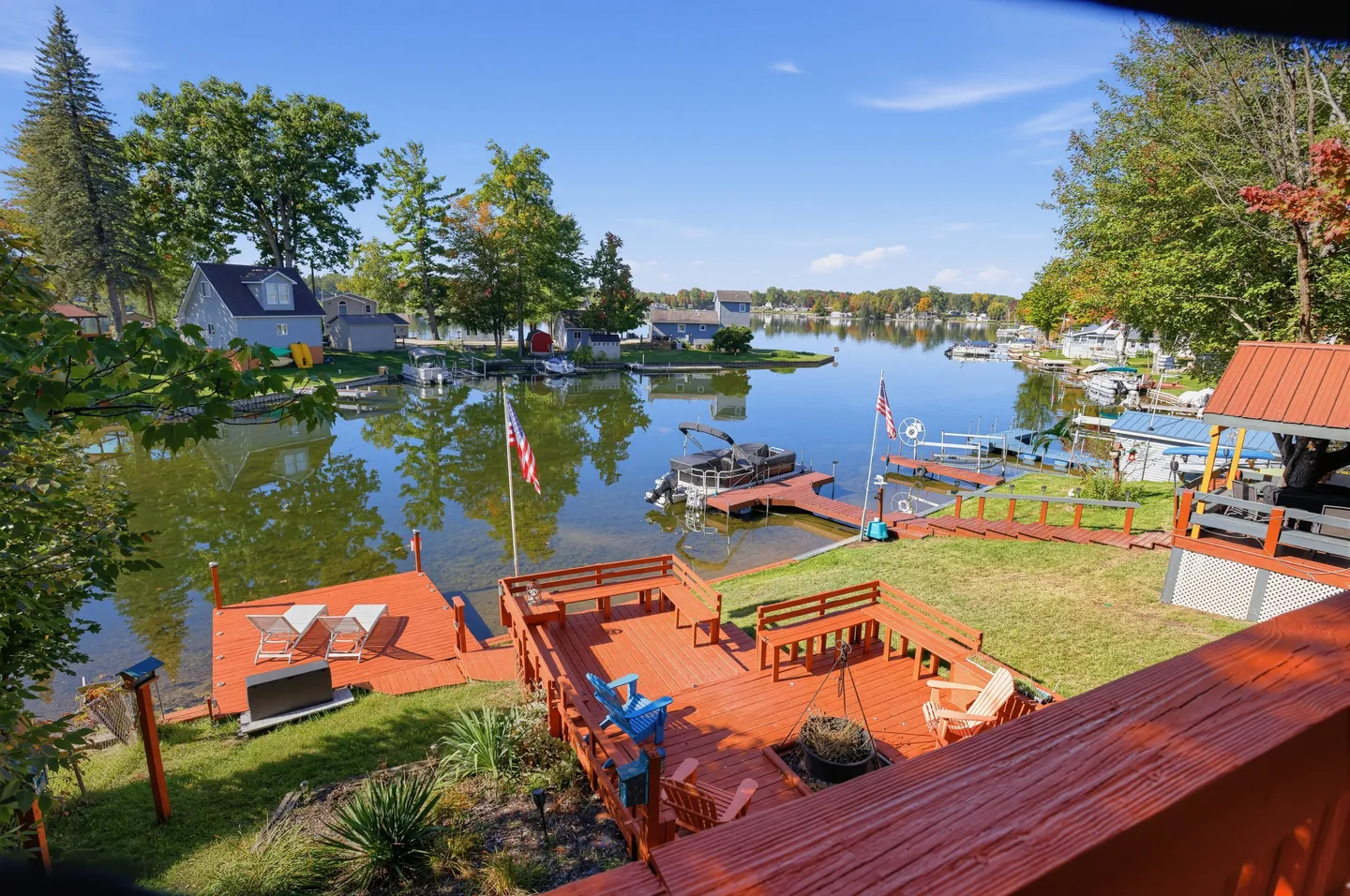 Elevated view of a lakeside deck, docks, and boats on calm water under a blue sky.