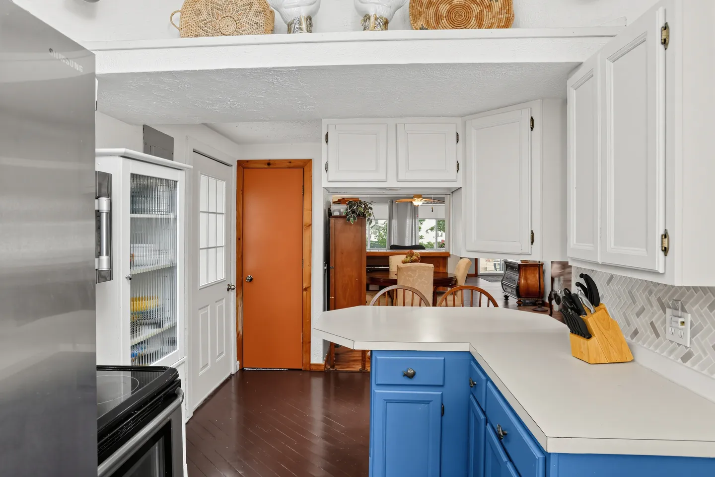 Kitchen counter with bright blue base cabinets, white upper cabinets, and dark flooring leading to an adjacent dining area.