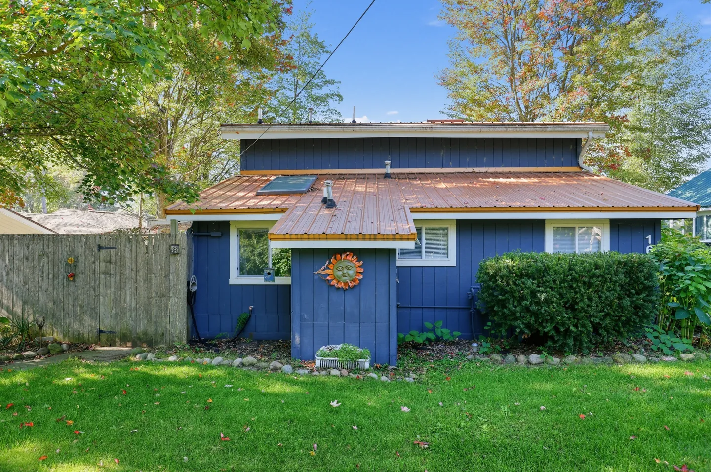 Exterior view of a blue-sided house with a copper-colored metal roof and a grassy lawn.