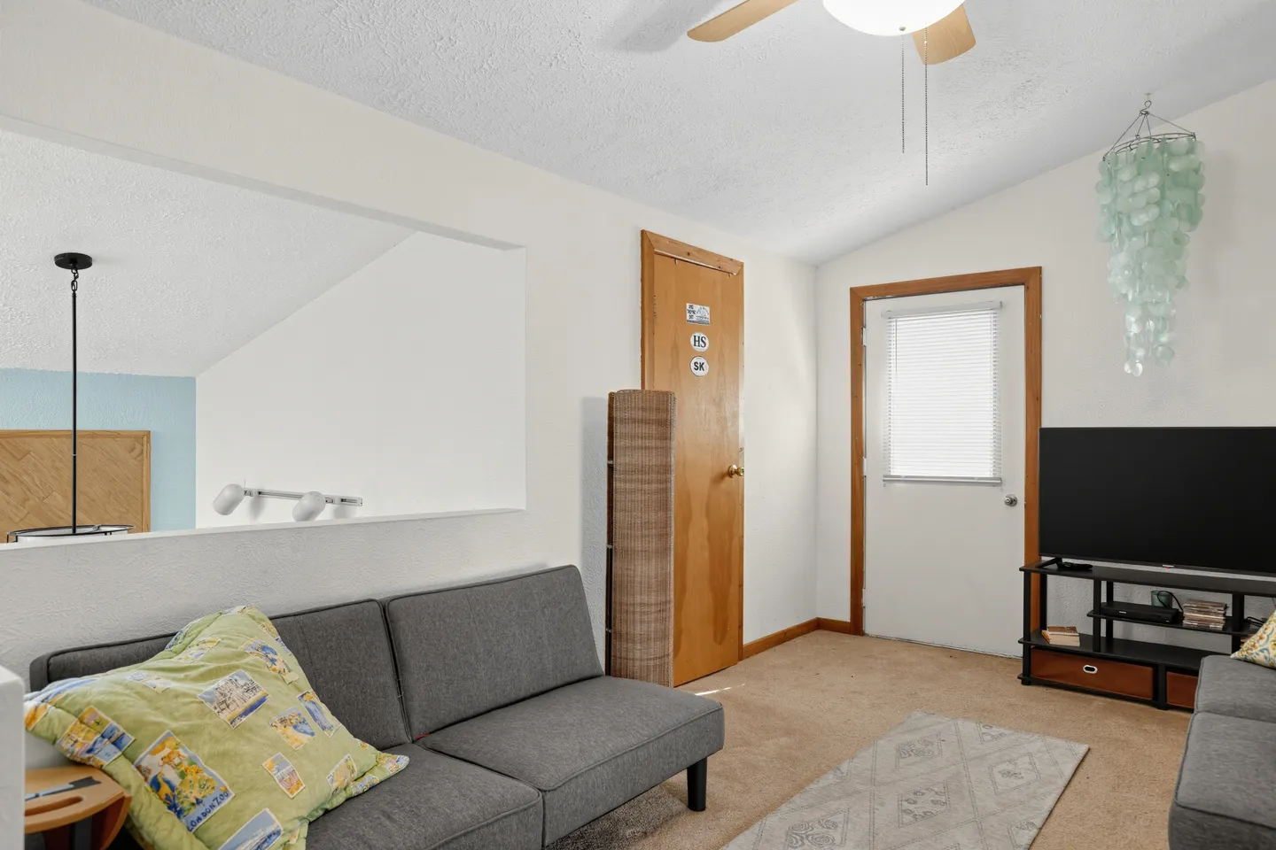 Upstairs loft sitting area with grey futons, a TV on a stand, carpeted floor, and a door.