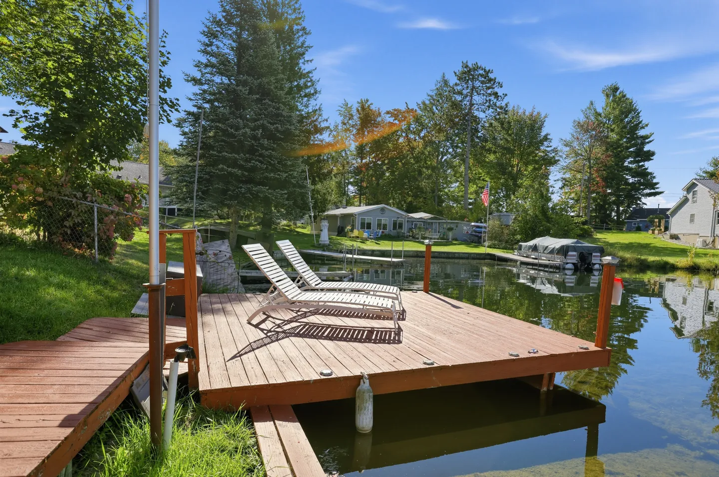 Wooden dock on a calm lake with two lounge chairs under a blue sky.