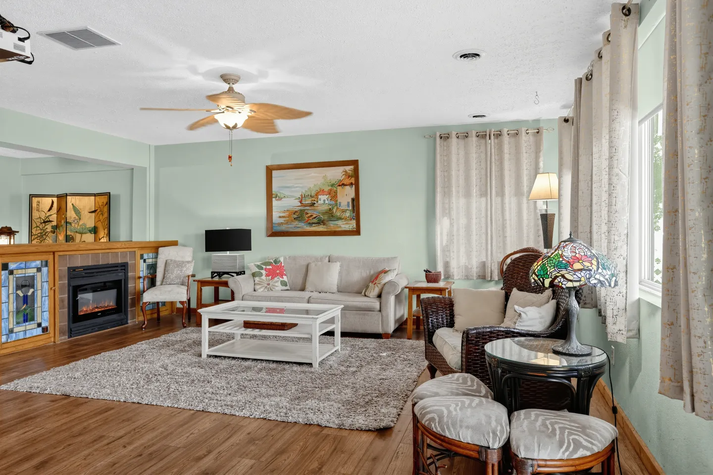 Living room with wood-look floors, a sofa, coffee table, area rug, wicker armchairs, and an electric fireplace built into a half-wall.