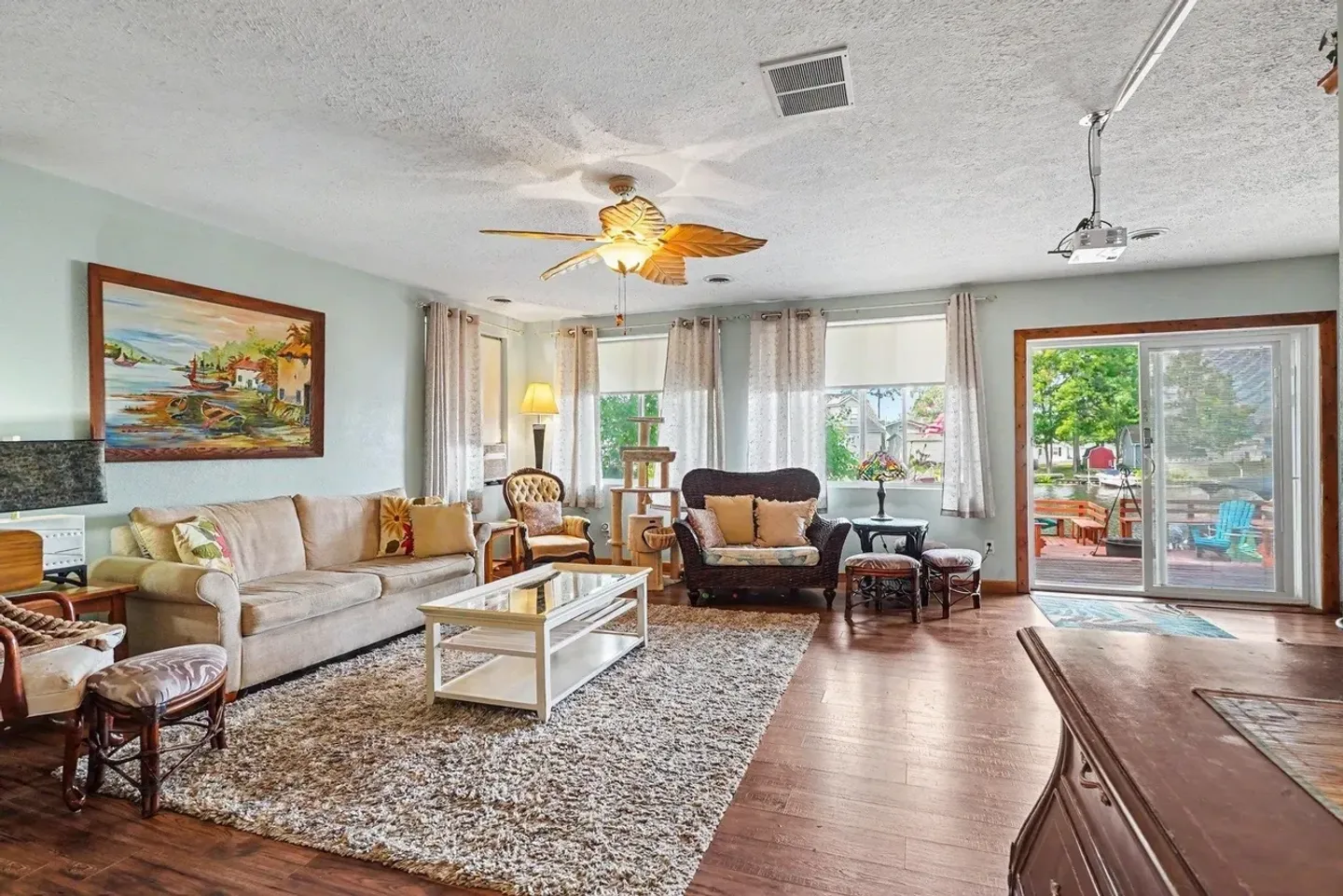 Living room with a beige sofa, coffee table, armchairs, ceiling fan, and sliding glass doors opening to an outdoor deck.