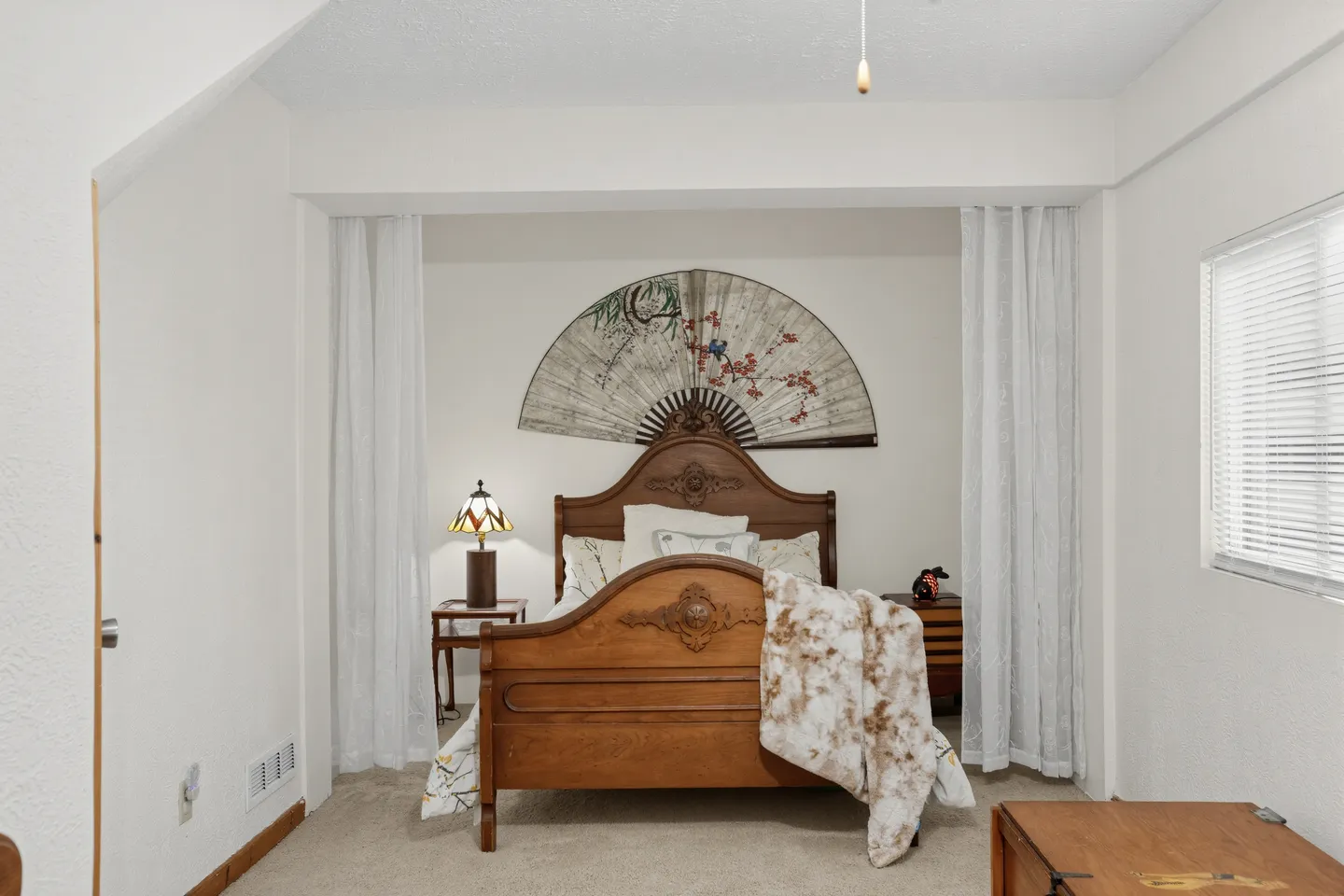 Bedroom alcove featuring a carved wooden bed beneath a large decorative folding fan hung on the wall.