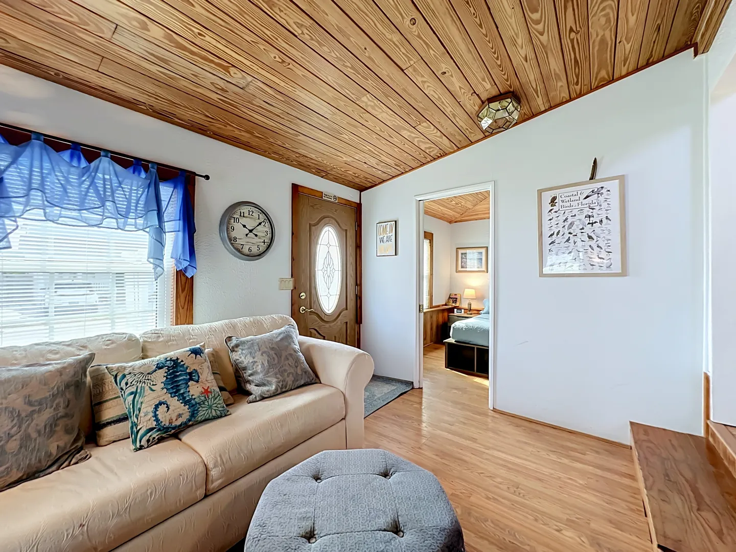 Living area featuring a couch, ottoman, wood-paneled ceiling, and a doorway leading to a bedroom.