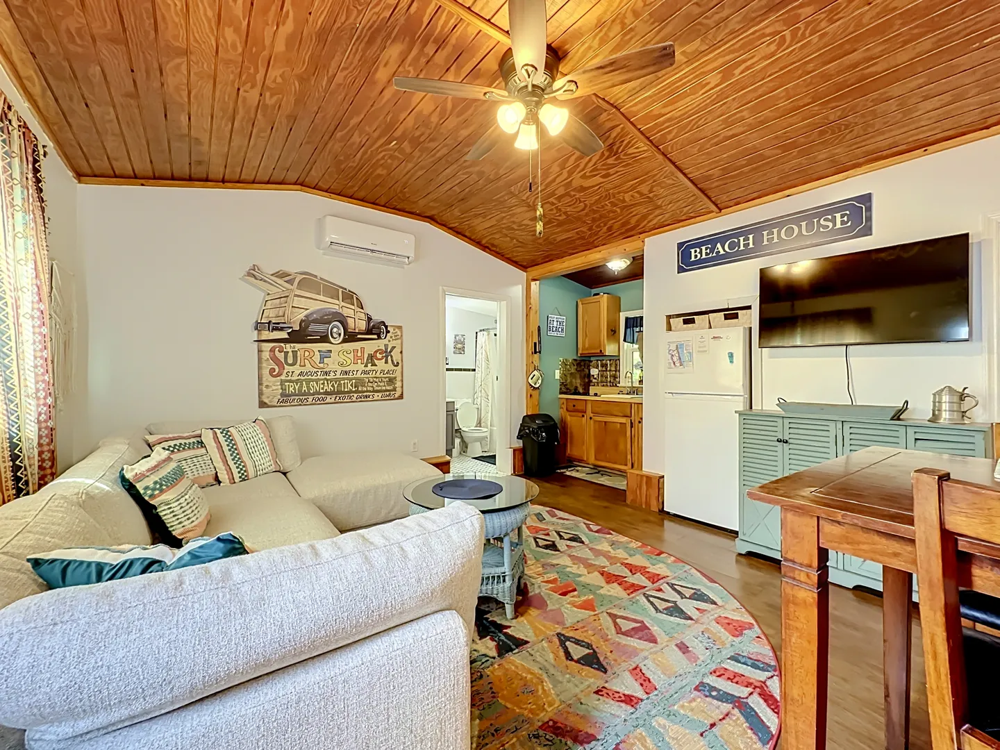 Living area featuring a sectional sofa, wood-paneled vaulted ceiling with a fan, television, and view into the kitchen.