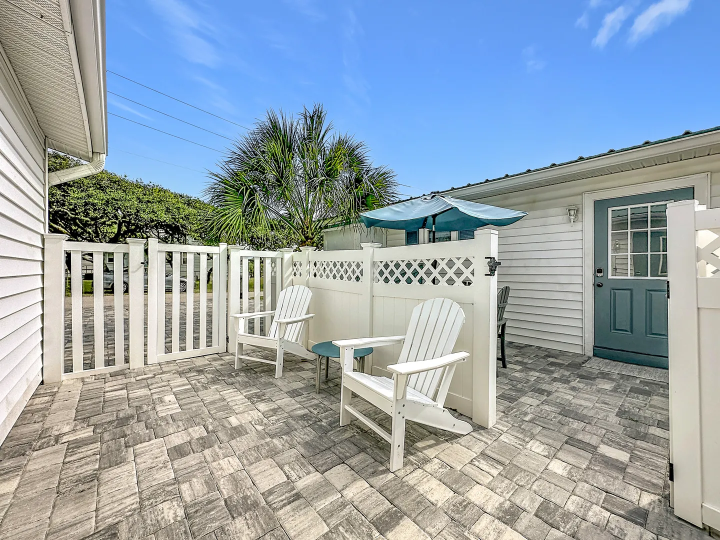 Enclosed outdoor patio paved with stone pavers, featuring two white Adirondack chairs and a privacy fence.