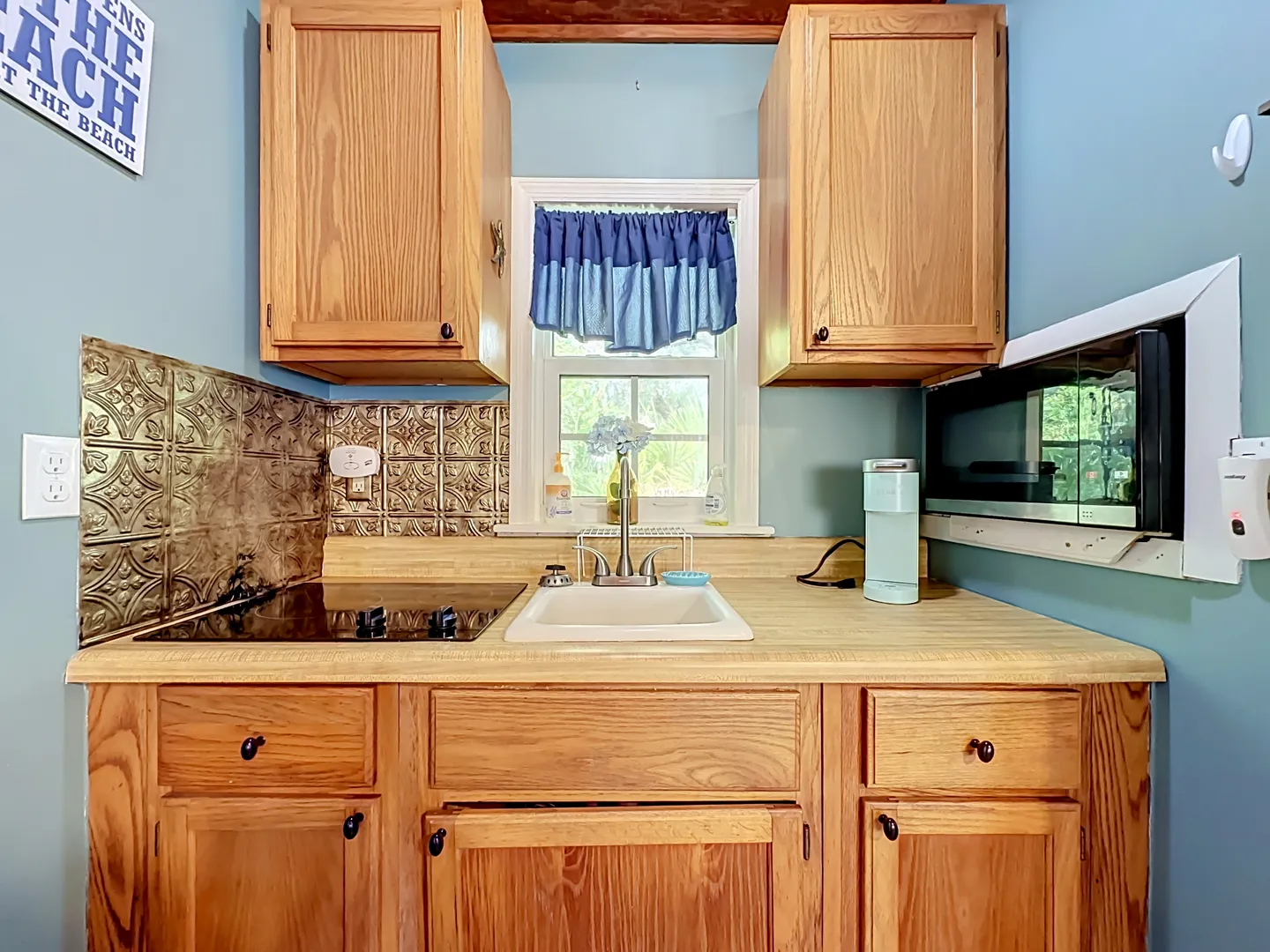 Compact kitchen area with light oak cabinets, a small sink, a two-burner cooktop, and a microwave.
