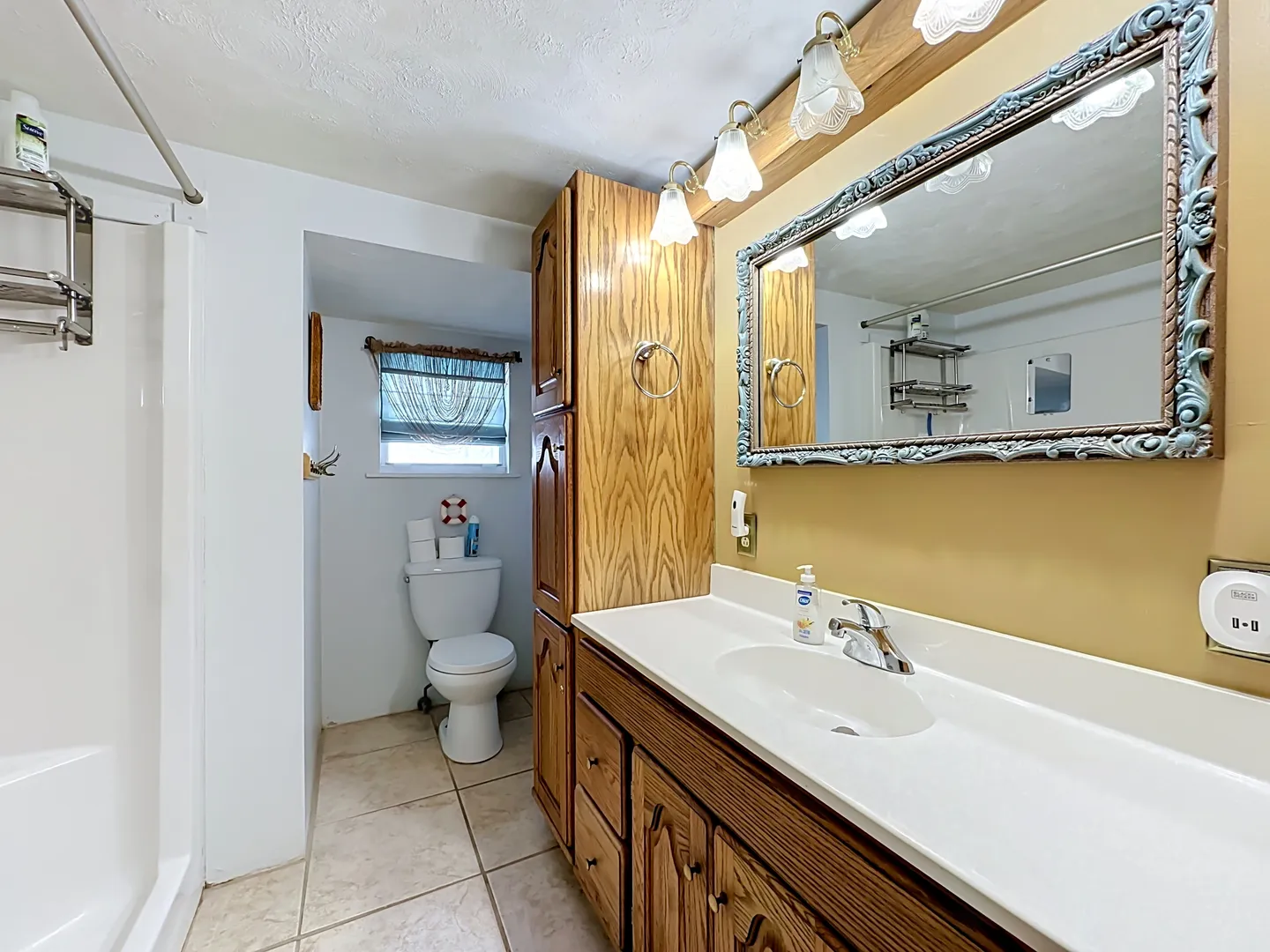 Bathroom with a wood vanity, white countertop, ornate framed mirror, and a toilet nook in the background.