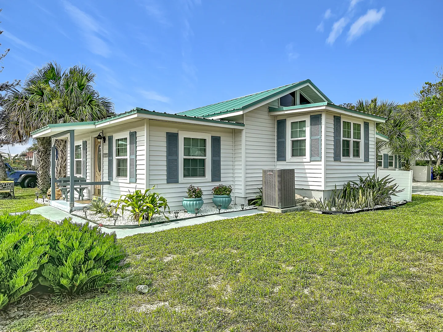 Exterior front view of a single-story home with light siding, a green metal roof, blue-gray shutters, and a grassy front lawn.