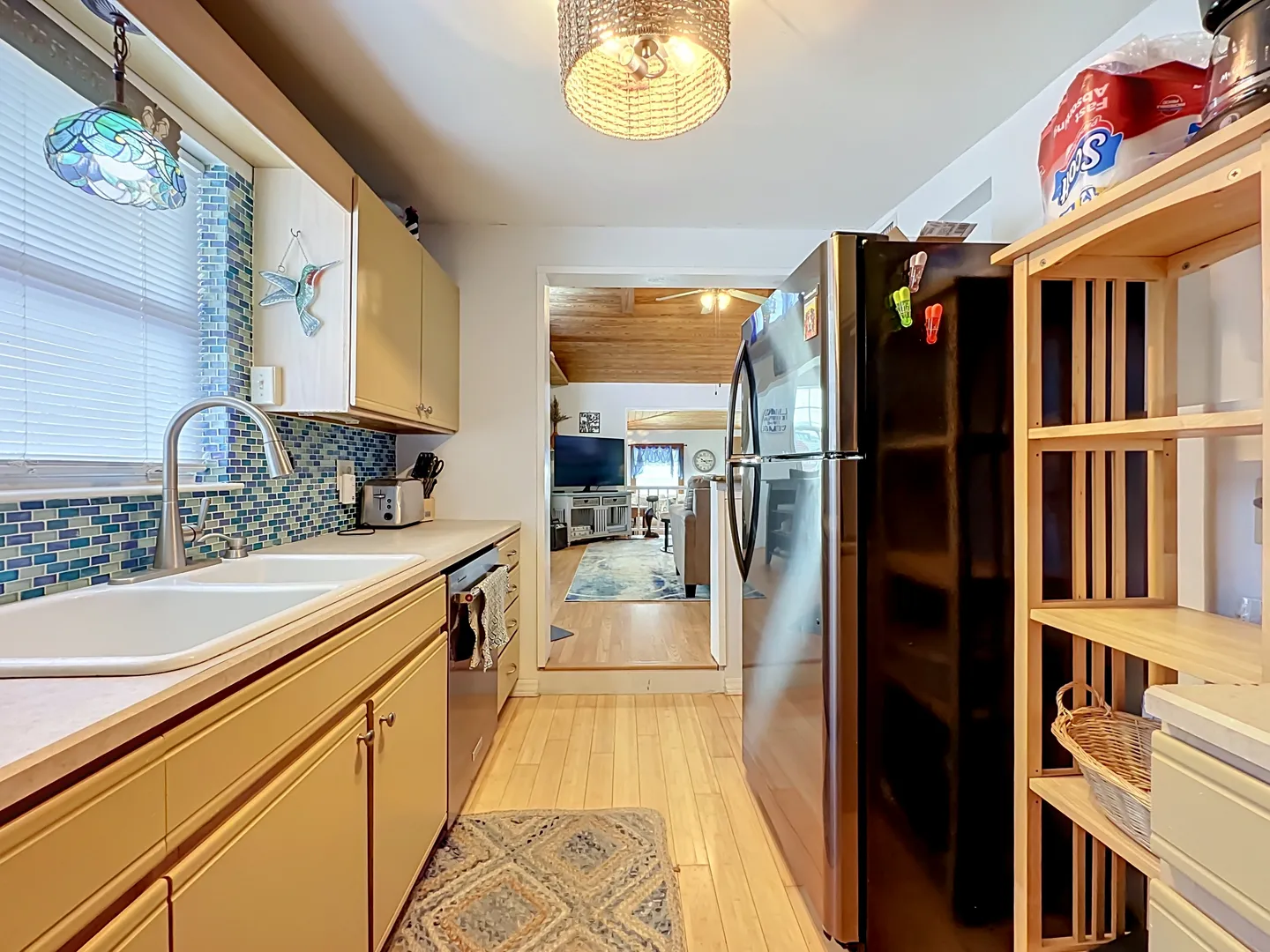 Galley kitchen with light cabinetry, blue tile backsplash, stainless steel appliances, and a view into the living room.