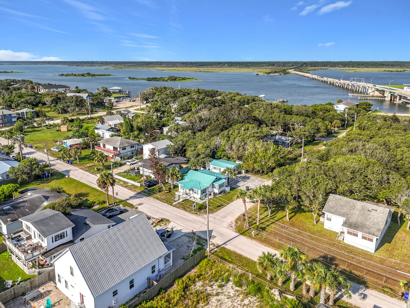 Aerial view of a coastal neighborhood with houses, trees, roads, and a large body of water crossed by a bridge.