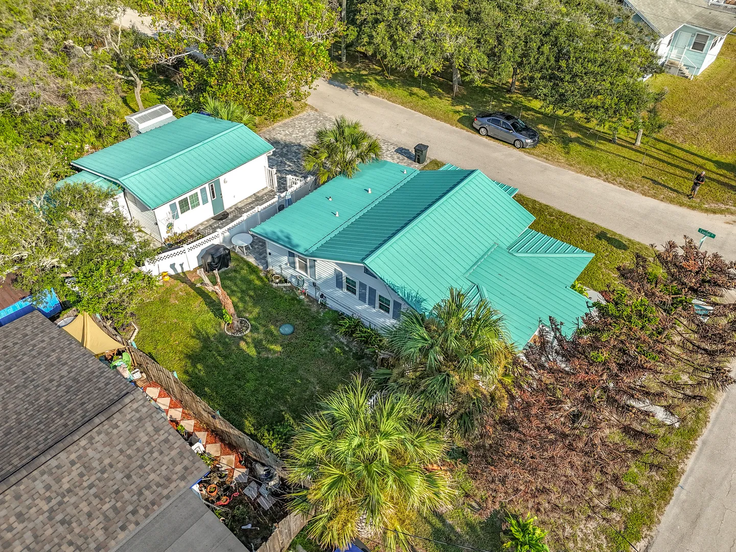 Aerial view of a coastal property featuring two white buildings with teal metal roofs and a grassy yard.