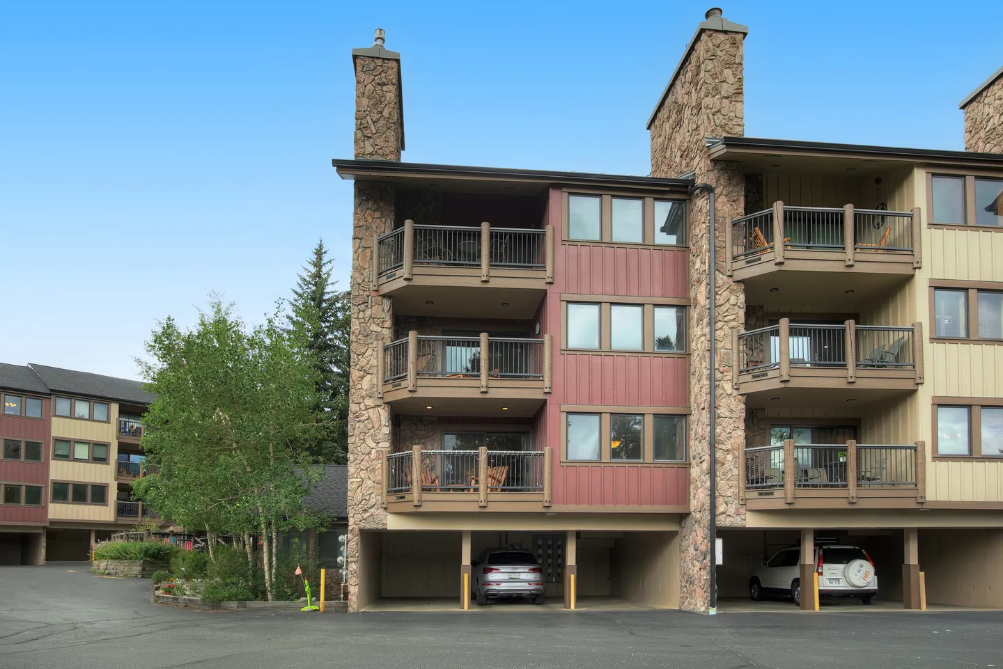 Exterior view of a multi-story condo building with stone chimneys, balconies, and ground-level covered parking.