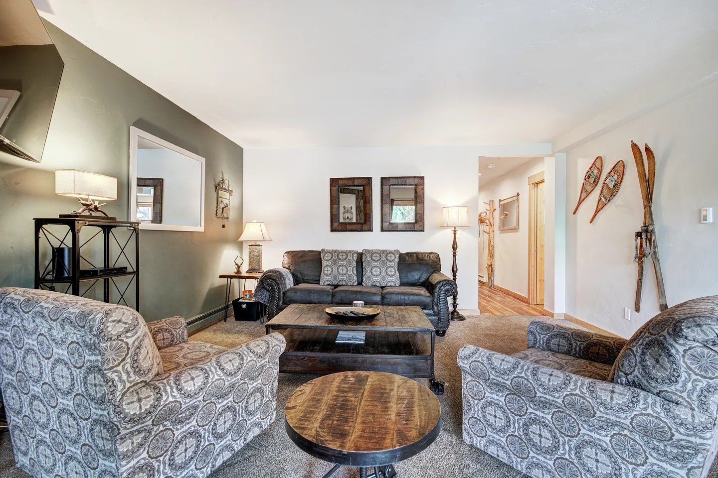Living room with patterned armchairs, a leather couch, wooden coffee tables, and winter sports decor mounted on the wall.