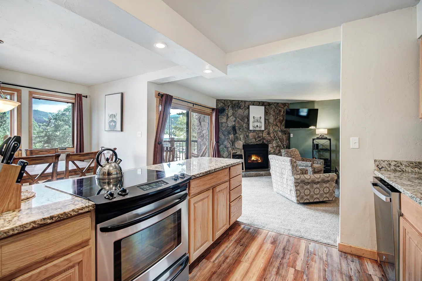 Open-concept kitchen looking into a carpeted living room with a stone fireplace and armchair.