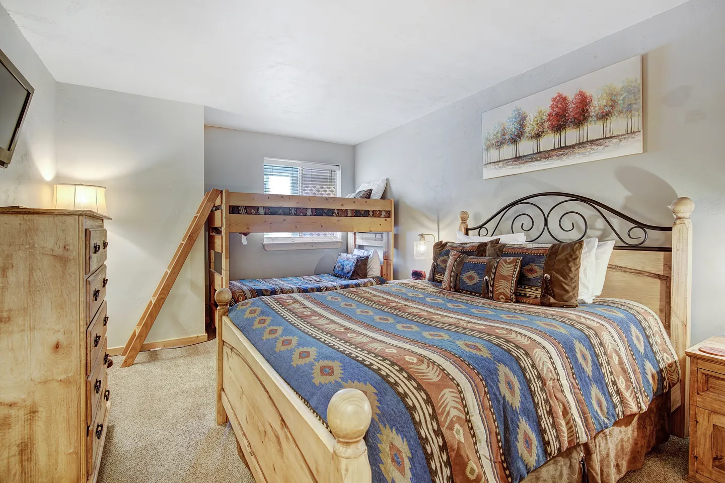 Bedroom with a large bed dressed in patterned southwest-style bedding alongside wooden bunk beds with an angled ladder.