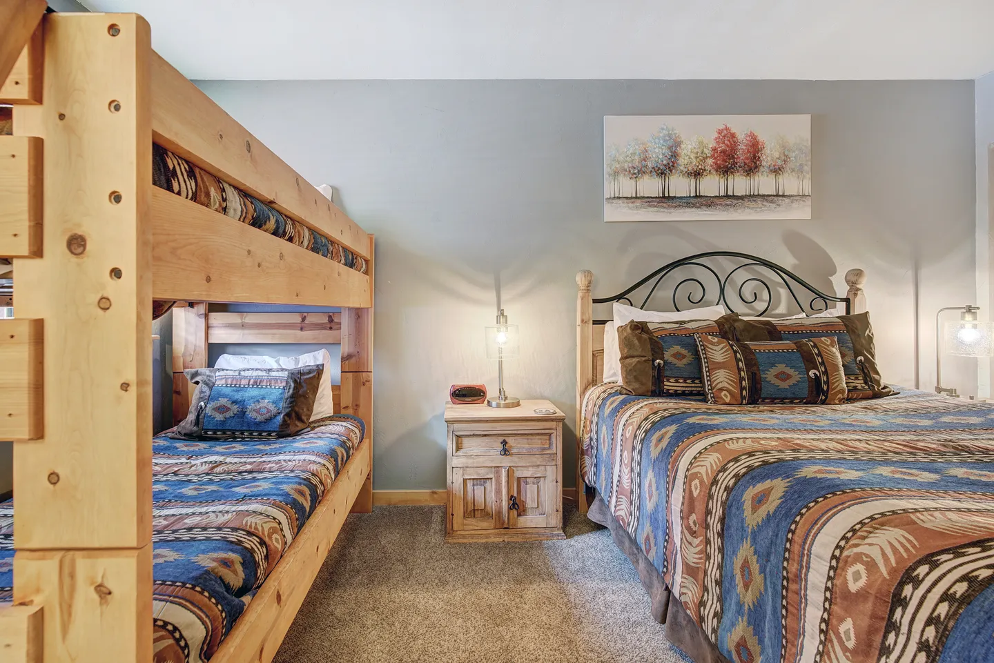 Bedroom with wooden bunk beds on the left and a queen-size bed on the right, separated by a nightstand.