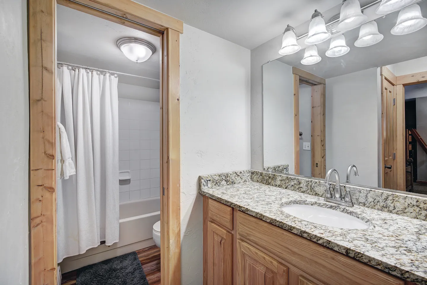 Bathroom with a wood vanity, granite countertop, large mirror with vanity lighting, and a view into a tub and shower area.