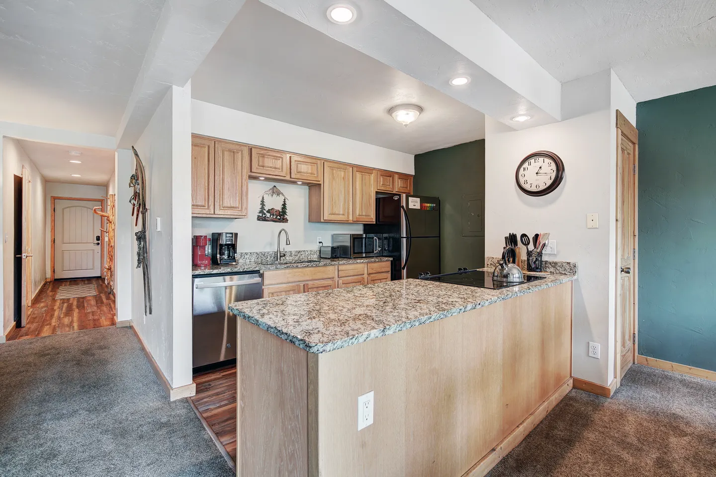 Kitchen with wooden cabinets, speckled countertops, kitchen island peninsula, and adjacent hallway with wood-look flooring.