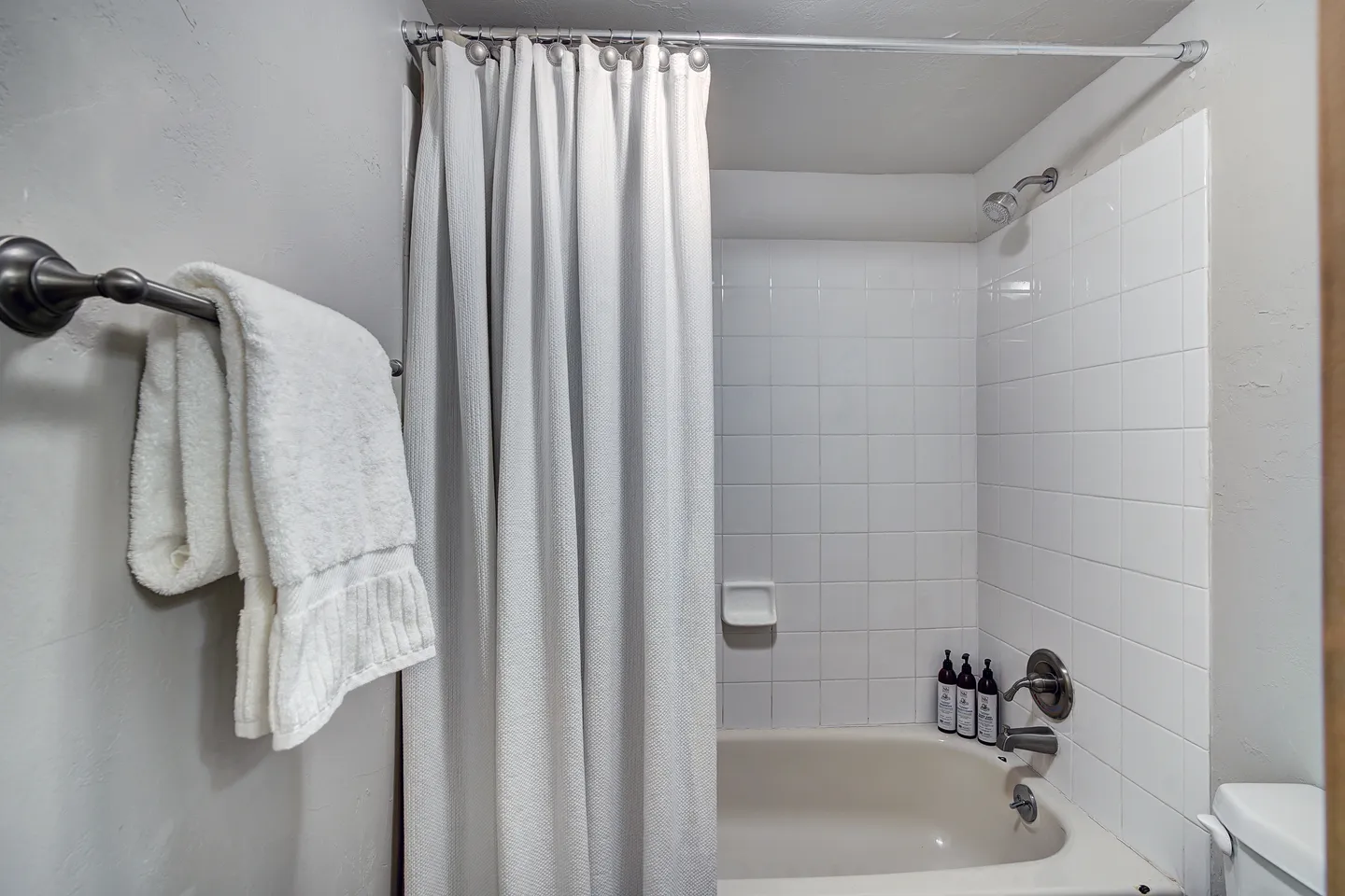 Bathroom bathtub and shower combination with white square tile surround, hanging shower curtain, and a towel bar with folded white towels.