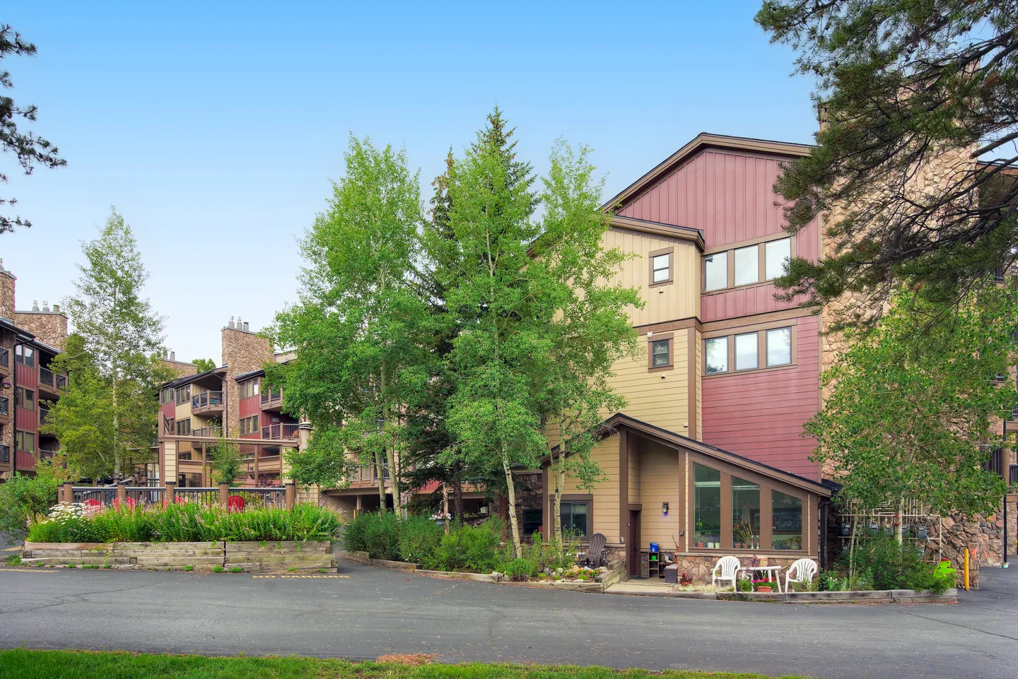 Exterior view of a multi-story lodge-style condominium building with wood and stone siding, surrounded by green trees and paved parking.