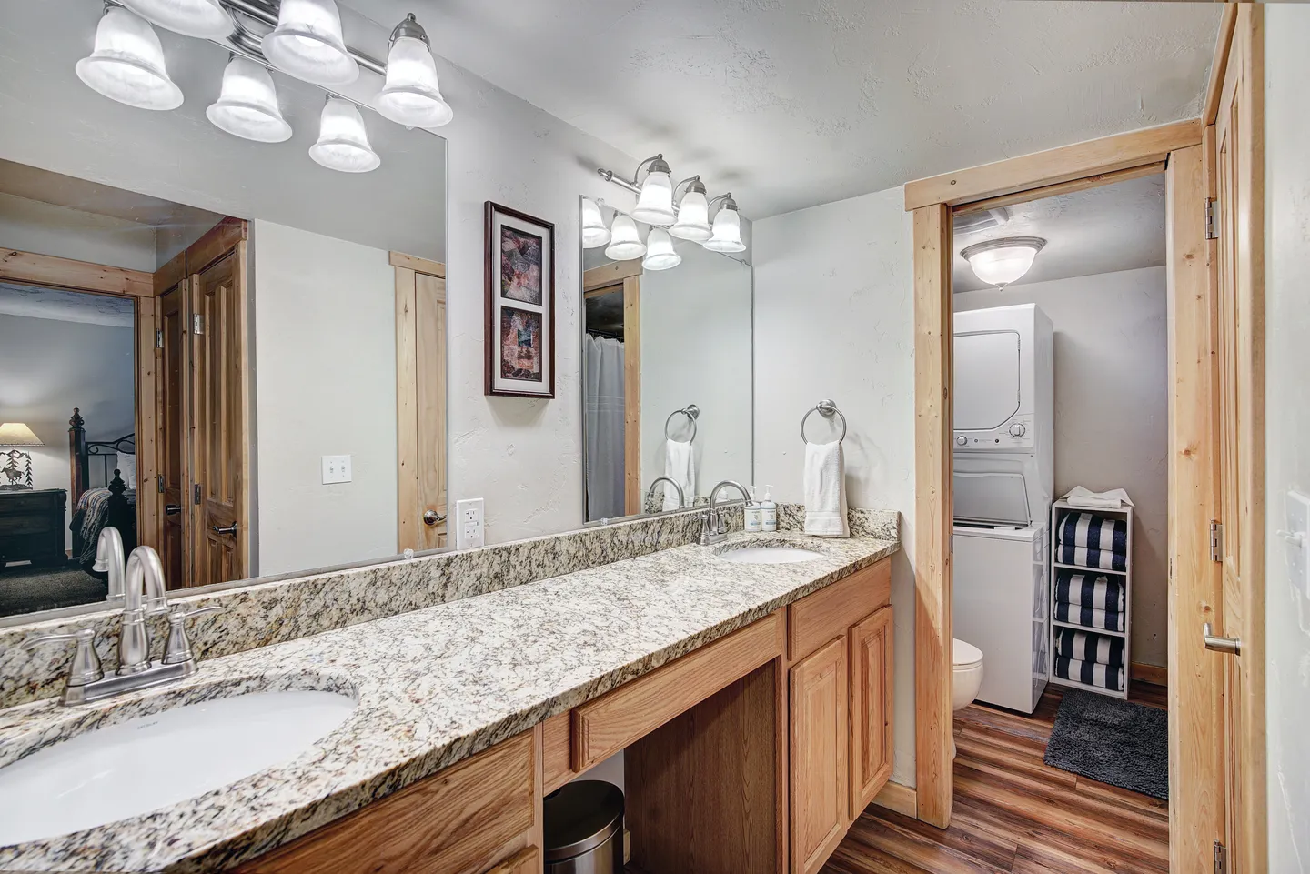 Bathroom with a long double-sink vanity and a doorway opening into a laundry area with stacked washer and dryer.