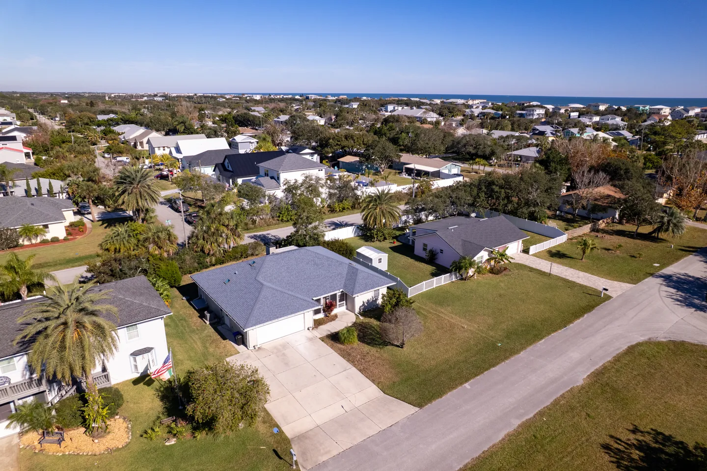 Aerial view of a single-story residential home with a wide driveway in a coastal neighborhood near the ocean.