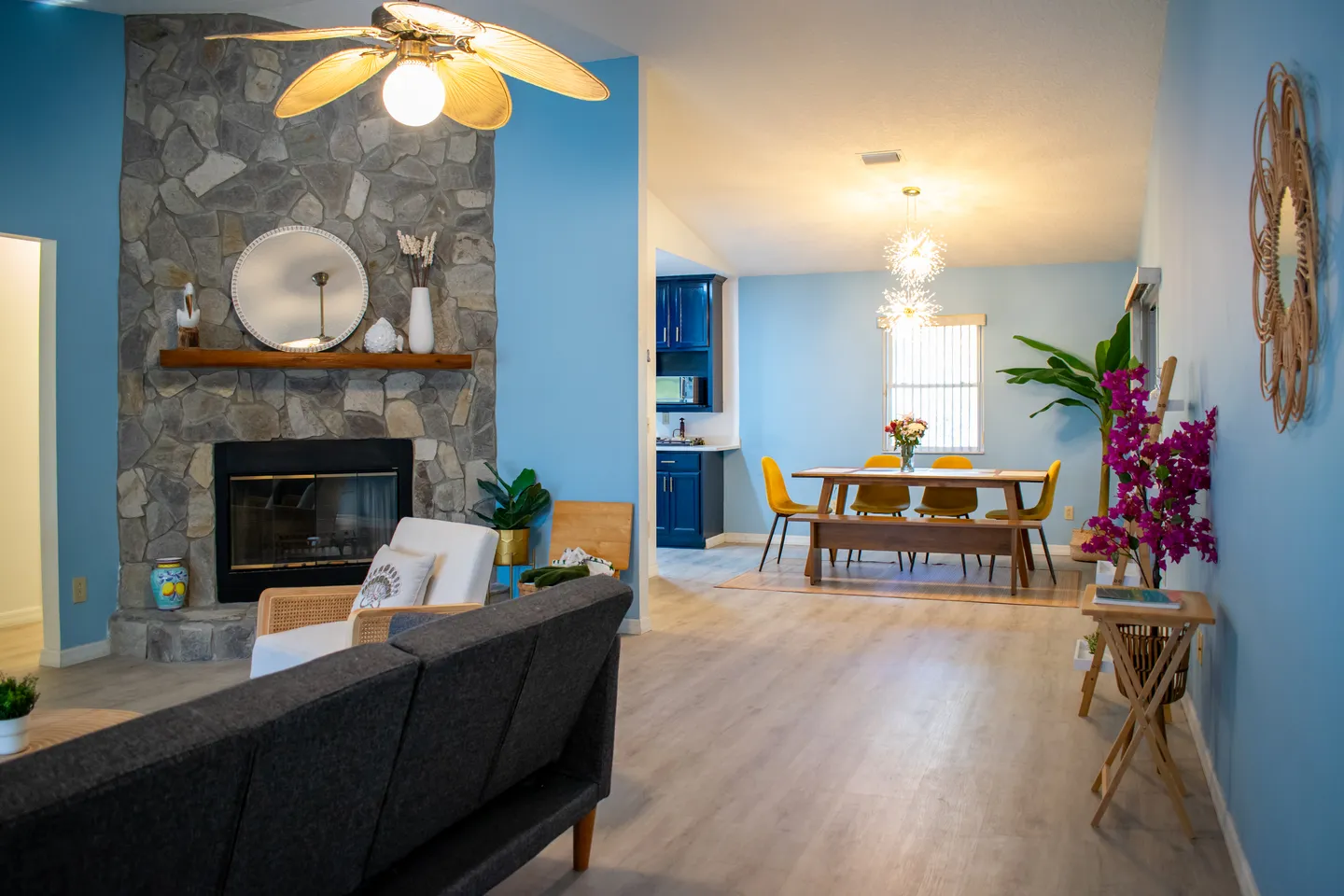 Open-concept living room and dining area featuring blue walls, a stone fireplace, and a dining table with chairs and a bench.