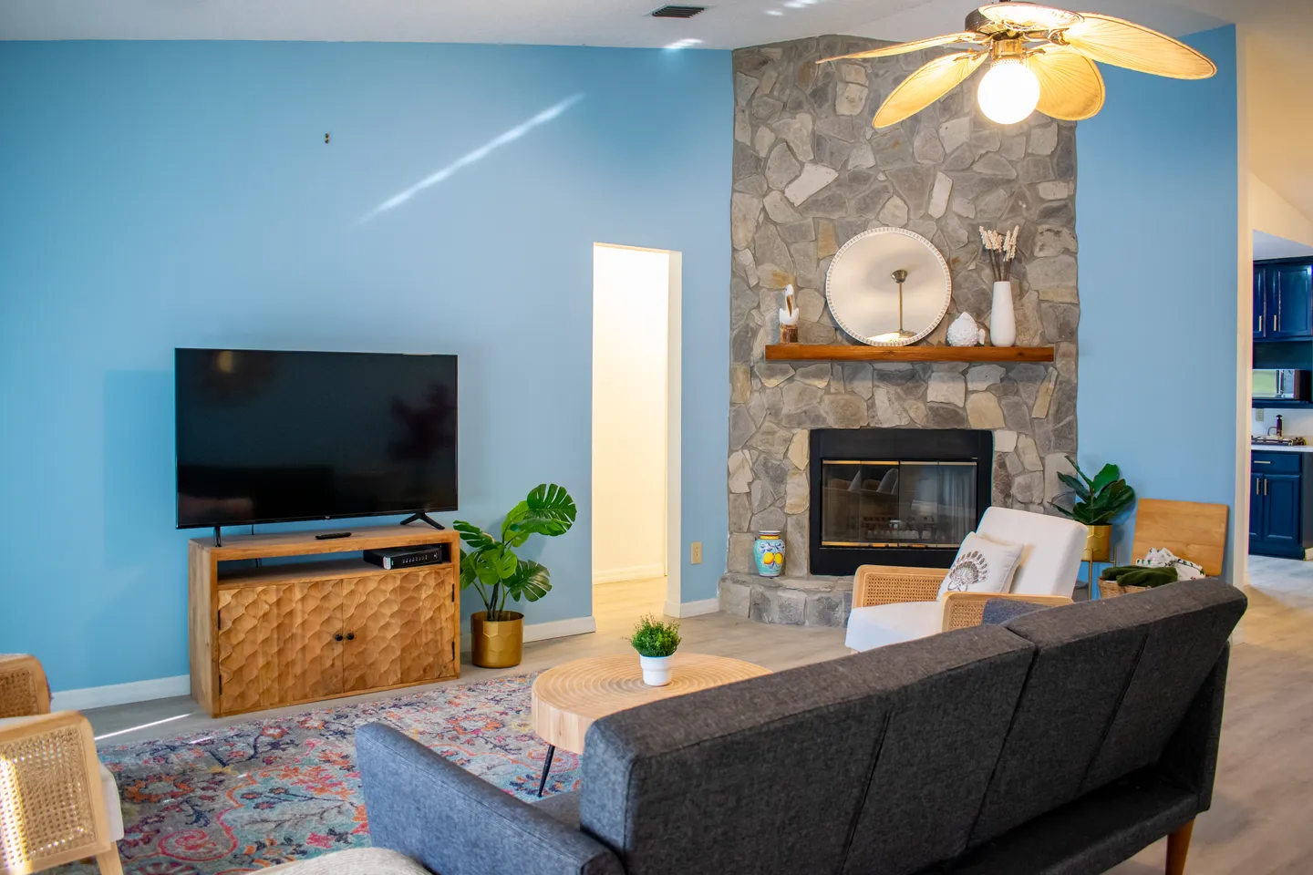 Living room with light blue walls, a stone corner fireplace, a flat-screen television on a console, and seating arranged around a coffee table.