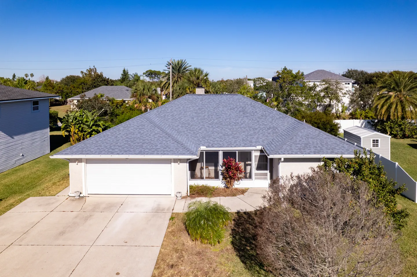 Elevated view of a single-story home with a blue-gray shingle roof, two-car garage, and concrete driveway under a clear sky.