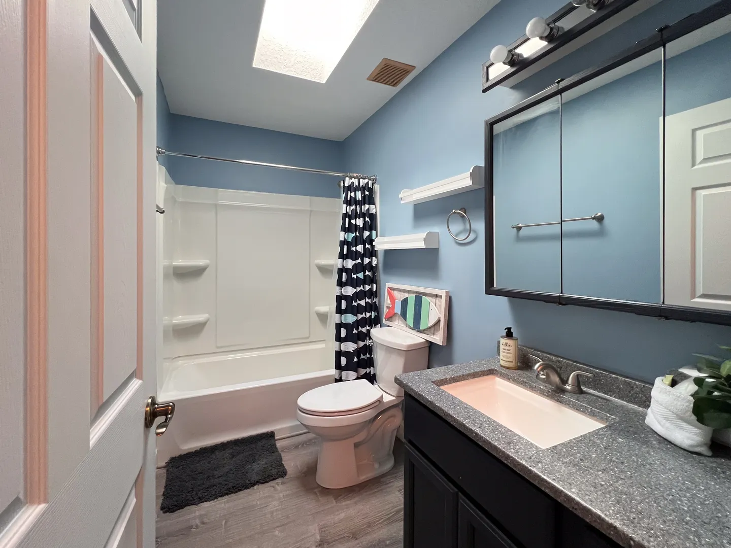 Bathroom with light blue walls, a white shower and tub combination, toilet, and vanity with a dark speckled countertop.