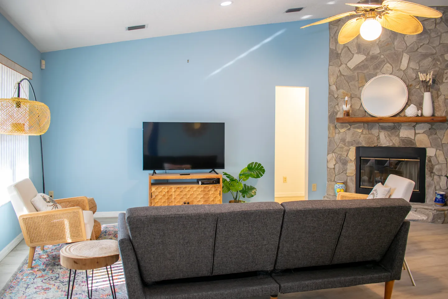 Living room with light blue wall, stone fireplace, flat-screen TV on a media console, and grey sofa.