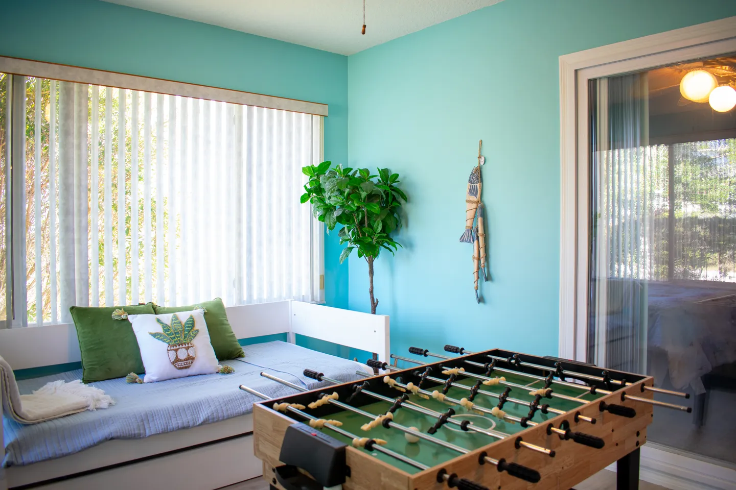 Sunroom or game room with aqua walls, a daybed, vertical blinds, and a foosball table.